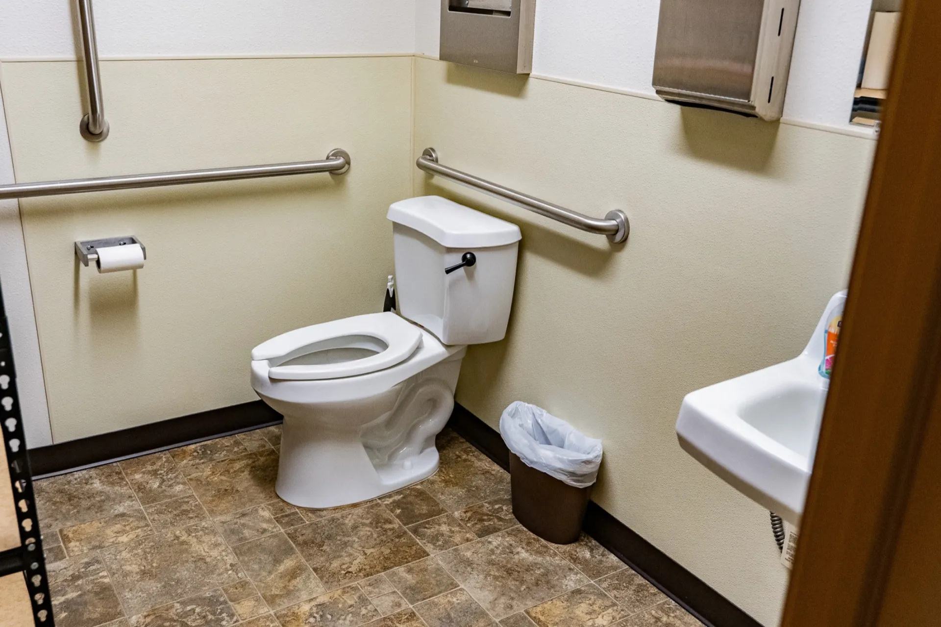 The same office restroom after cleaning, with a fresh liner, clear floors, and polished fixtures