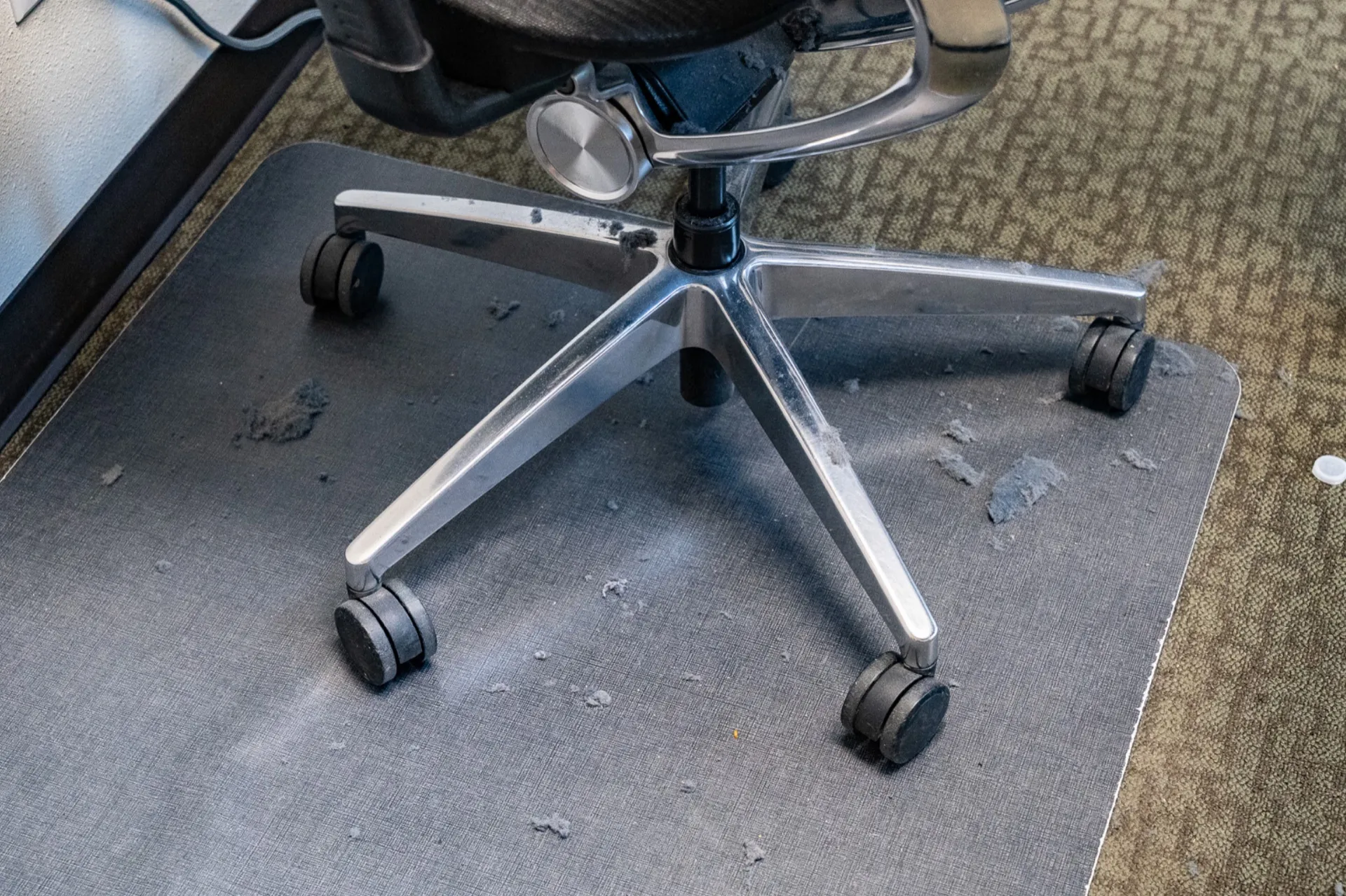 Office chair base covered in dust bunnies on a chair mat before cleaning